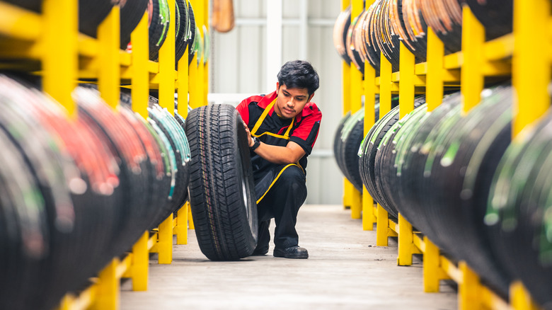 mechanic leaning a tire against a warehouse shelf lined with more tires
