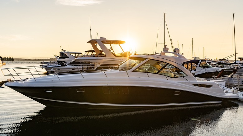 A luxury boat docked at a marina during with the sunset and other boats behind it.