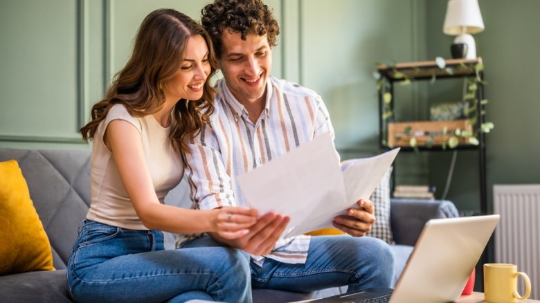 A young couple sits on a couch looking at financial documents