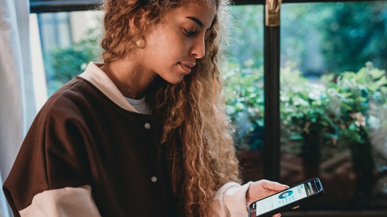 A young Gen Z woman looking at her financial portfolio on her phone.
