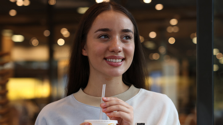 A smiling Gen Z woman sitting in McDonalds while holding a drink.