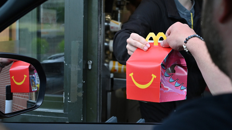 A man at a drive-thru window picking up a McDonald's Happy Meal.