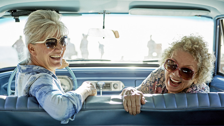 Two mature women looking back and smiling from the front seat of a classic car