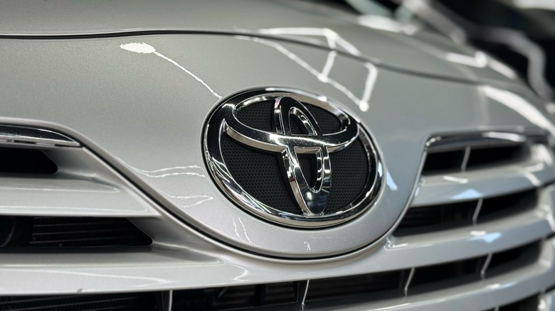 Close-up of a silver Toyota Camry's front grille, with the Toyota emblem centered and garage lights reflecting across the hood