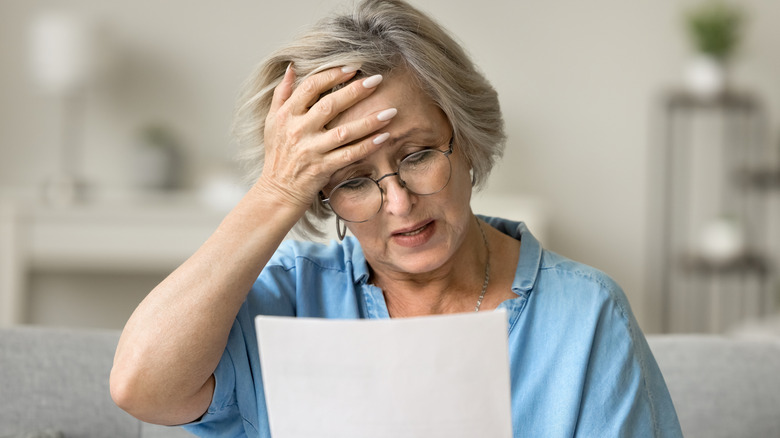 Stressed frustrated older woman getting bad news from paper letter,