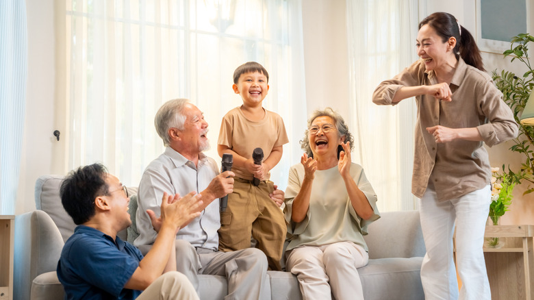 Happy Asian three generation family have fun singing and dancing together in living room.