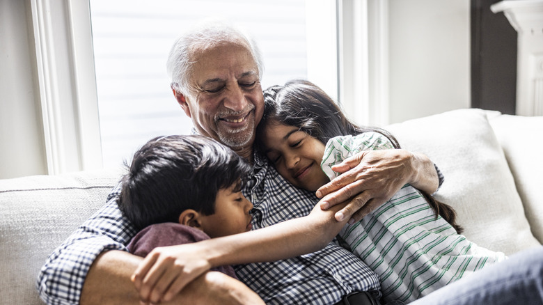 Grandfather cuddling with grandchildren on couch at home
