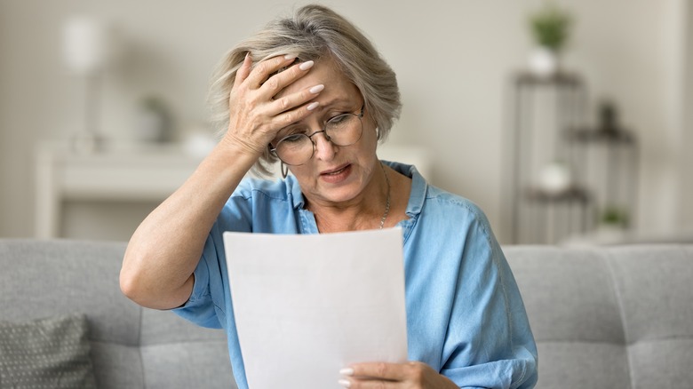 Stressed frustrated older woman getting bad news from paper letter,