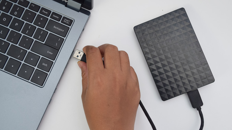 person plugging a hard drive into a USB port on a laptop