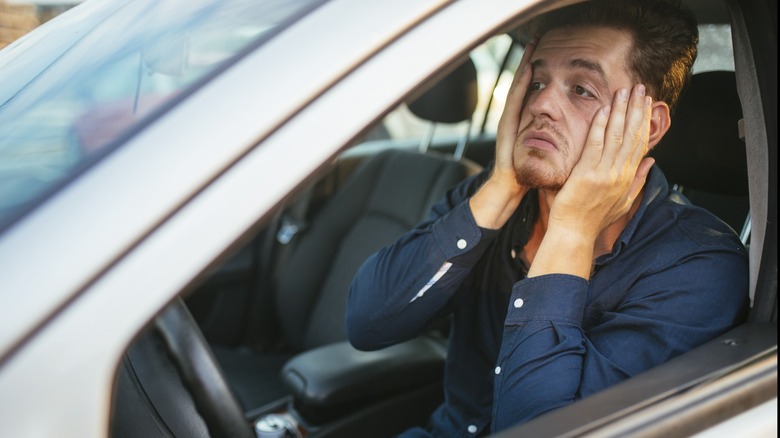 Worried man sitting behind the wheel of a car with his face resting in his hands