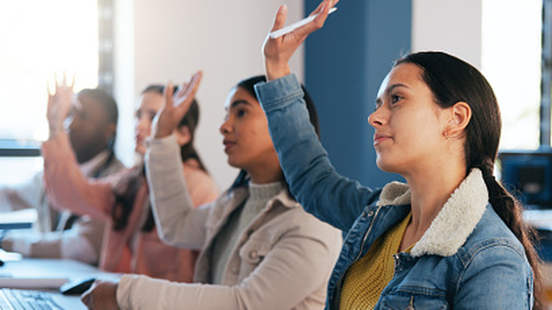 A row of driving-age students raising their hands in class