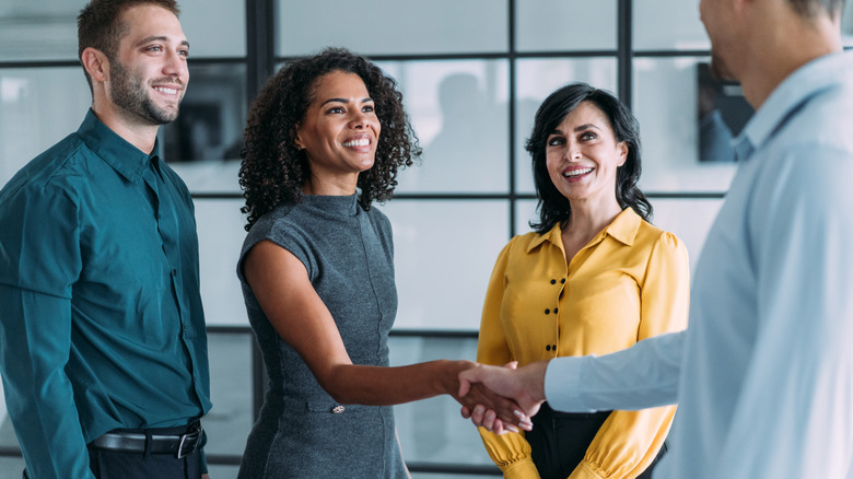 Group of people smiling in office setting as professional man and woman shake hands