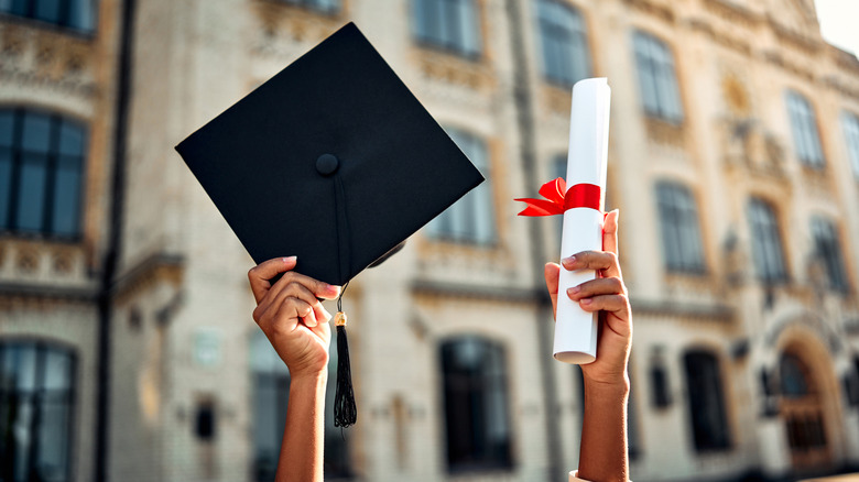 Cropped image of person holding graduation  cap and degree in the air