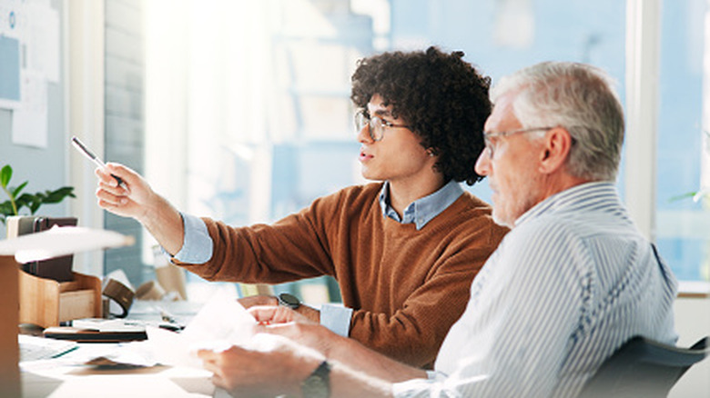Young and old business professionals speak seriously, seated in left-facing side profile