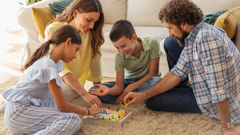 A Man, woman, boy, and girl sit on the living room floor playing a boardgame