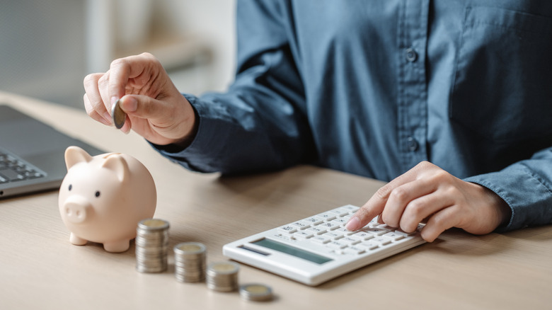 Person using calculator and putting coins in piggy bank