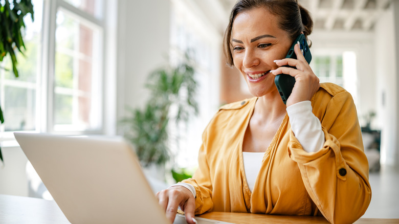 Woman working on laptop while talking on phone