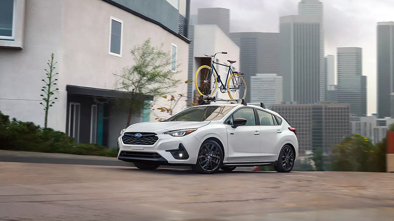 white 2026 Subaru Impreza with a bike on its roof parked on city street