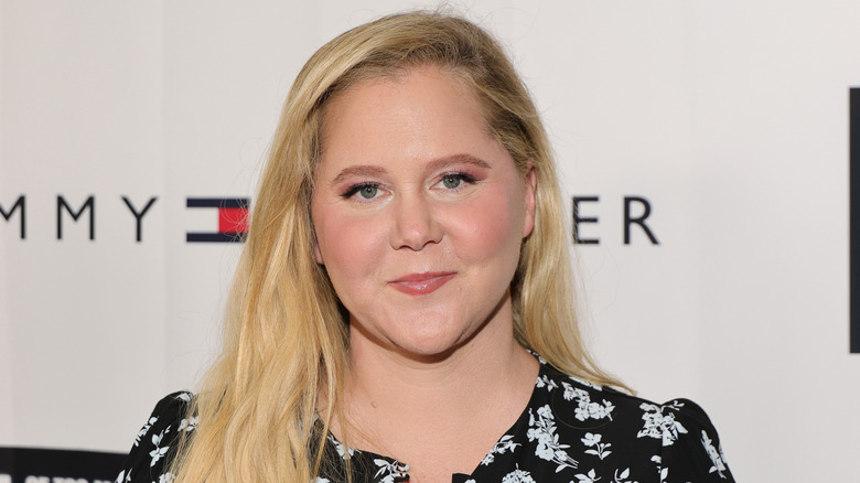 Amy Schumer smiling in front of white Tommy Hilfiger back drop