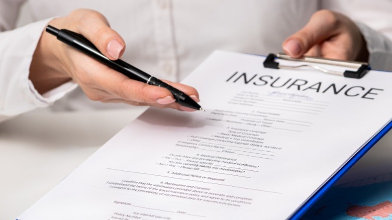 A doctor's hands holding a health insurance form on a clipboard in a medical office.