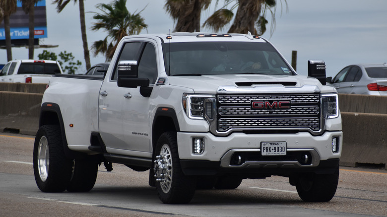 A portrait of a white GMC Sierra 3500 HD pick-up truck traveling down a highway in moderate traffic