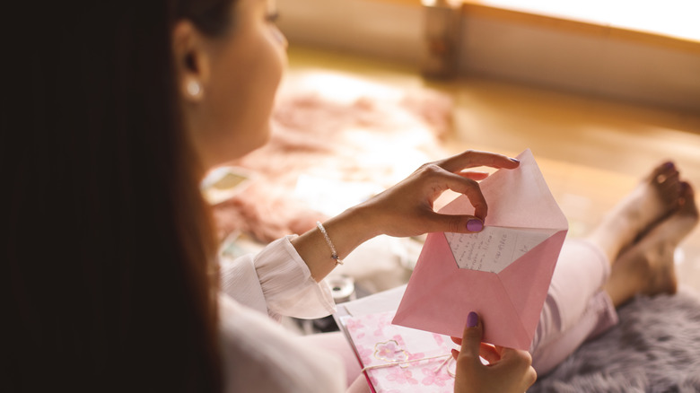 A young woman sitting on the bedroom floor and opening a love letter.