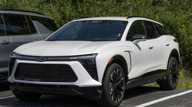 A white Chevy Blazer in a parking space next to some bushes.
