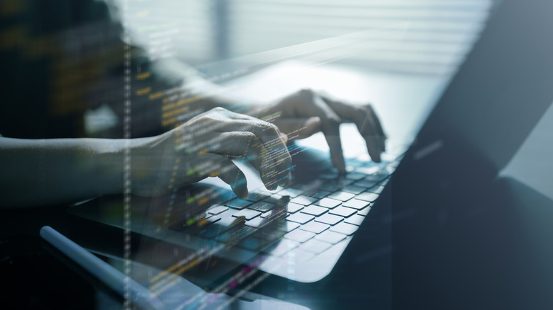 A programmer's hands typing on a laptop with programming graphics overlaid