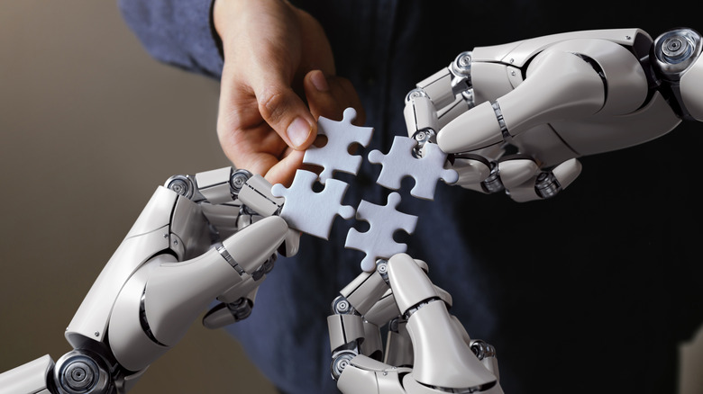 A human hand and three robot hands holding interlocking puzzle pieces