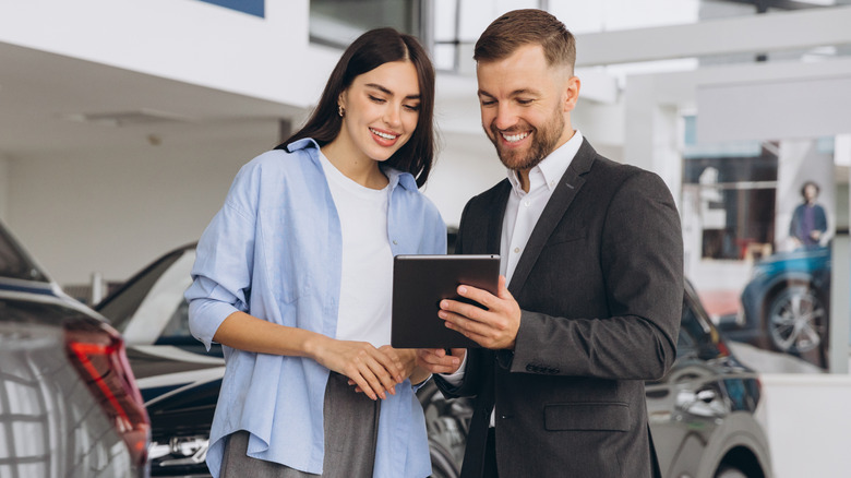 Young woman looking at car salesman's tablet