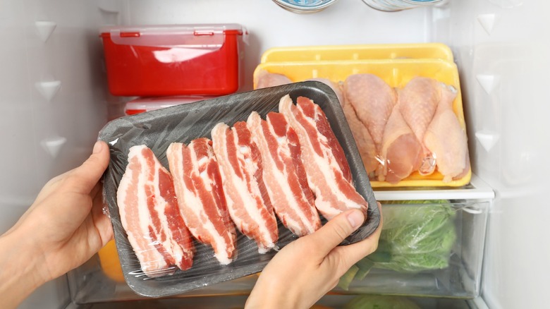 A pair of feminine hands placing a pack of bacon in a fridge