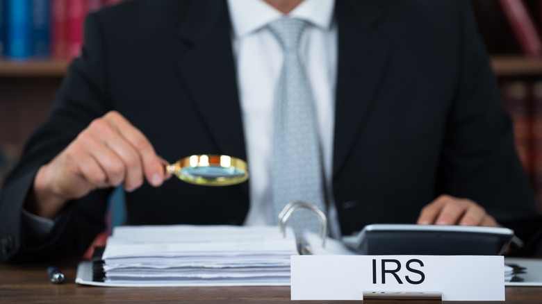 A man in a suit and tie sitting at a desk behind an IRS name plate