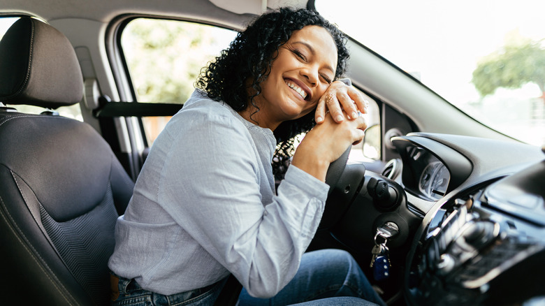 Young and cheerful woman enjoying new car hugging steering wheel sitting inside.