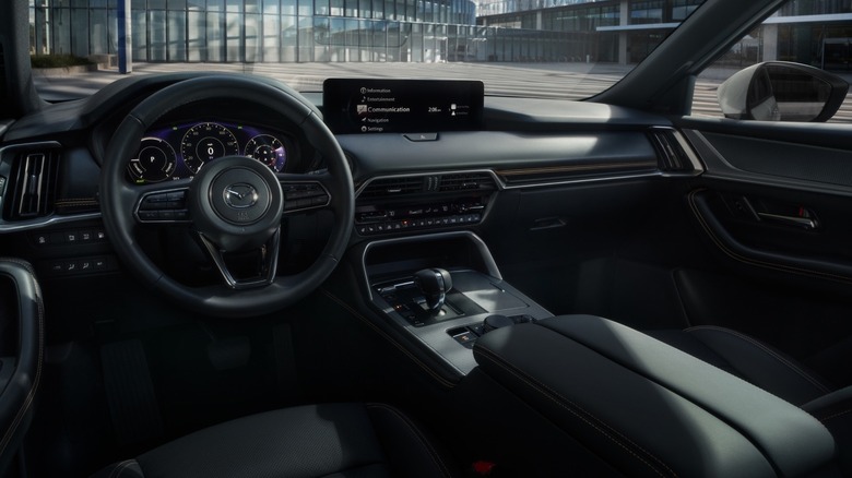 An interior image of the Mazda CX-90 PHEV with the steering wheel and infotainment screen visible.