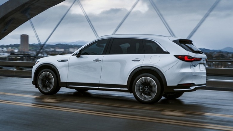 A white Mazda CX-90 PHEV driving on the highway across a bridge.
