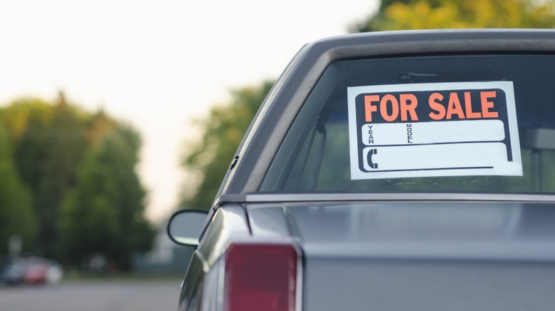 A for sale sign in the back window of a gray truck on the road.
