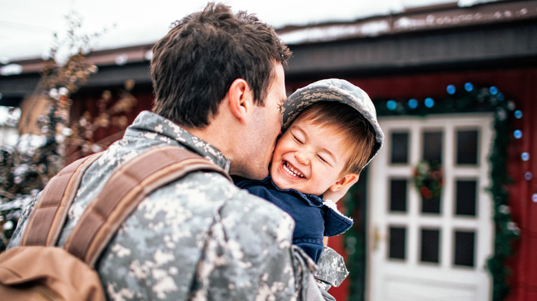 A returning soldier embracing a young boy outside their home.
