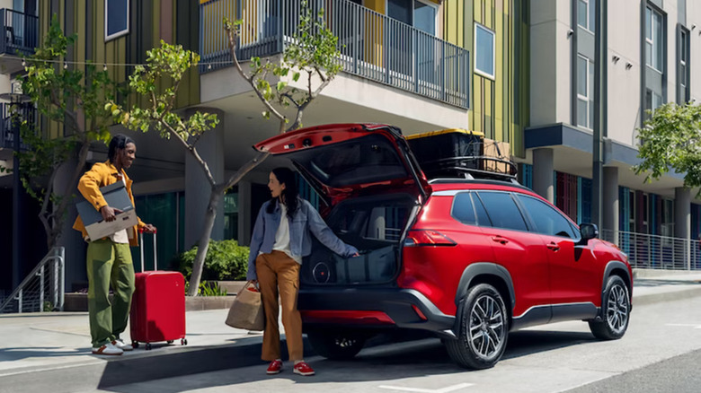a young couple packs luggage into the back of a red 2026 Toyota Corolla Cross