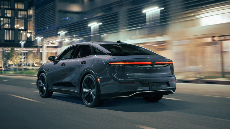 silver-gray 2026 Toyota Crown moves along nighttime city street in front of blurred well-lit modern buildings