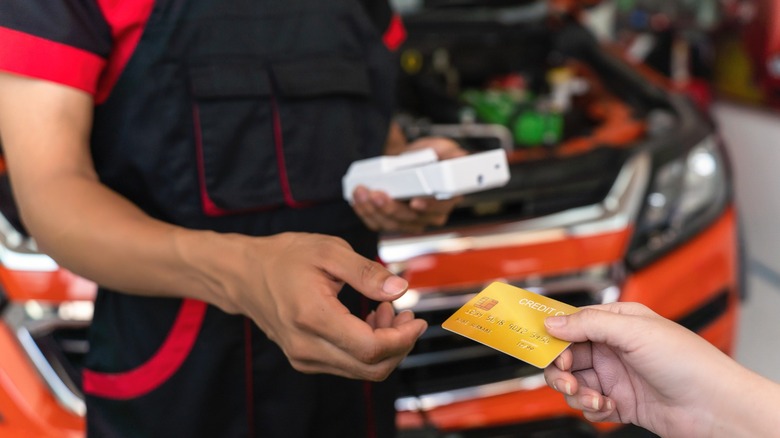 Mechanic receiving a credit card from a customer in front of a car with its hood open