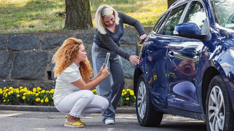 Two women inspecting damage on a car