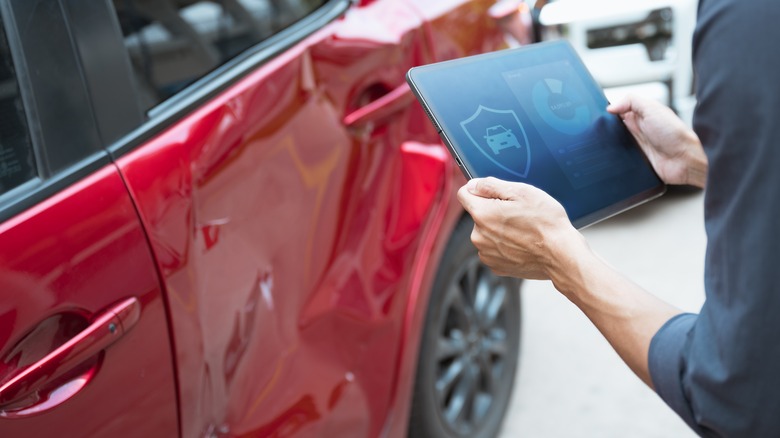 Person holding a tablet next to a damaged automobile