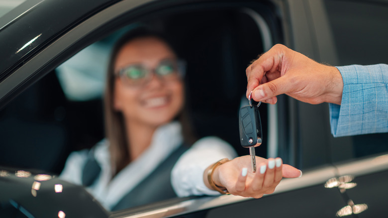 Smiling woman holds hand out for keys from dealer