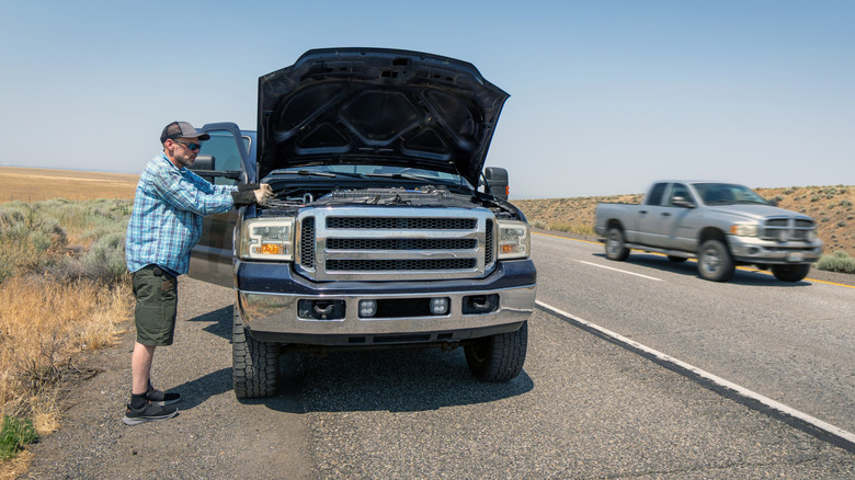 Man looking at the engine of a broken-down pickup
