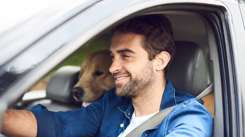 Man smiling while driving with dog in back seat