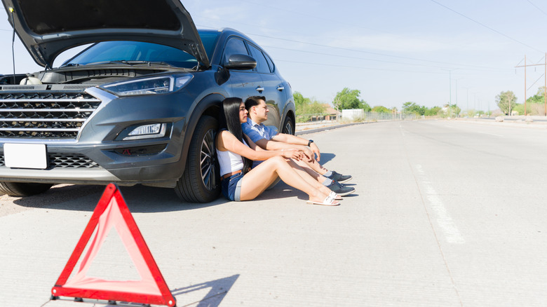 Couple sitting near a broken down car