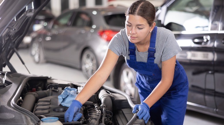 a female mechanic in overalls and gloves works on a car engine