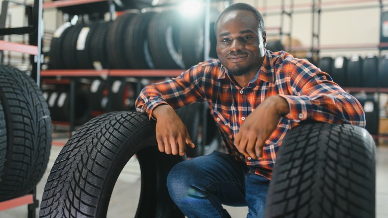 a man crouches with elbows resting on two tires