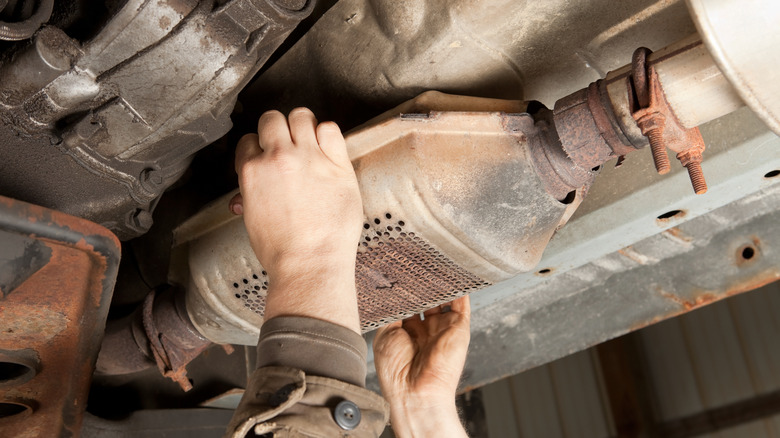 the hands of a mechanic removing a catalytic converter