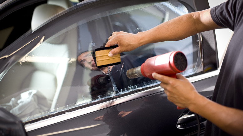 a technician uses a heat gun to apply car window tinting